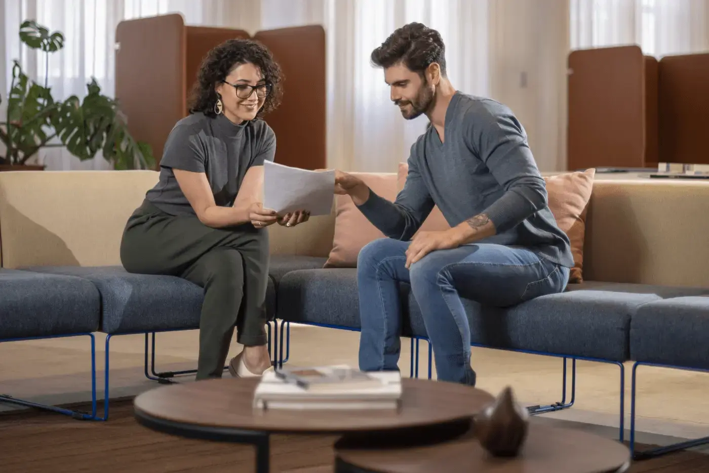 Duas pessoas sentadas em assentos acolchoados discutindo sobre papéis.
